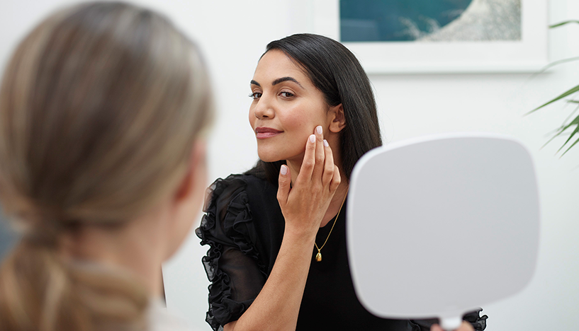 femme qui regarde son visage après injections d'acide hyaluronique de Juvederm une solution anti age